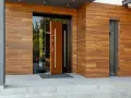 Eleganckie, brązowe barańskie drzwi zewnętrzne z drewnianą okładziną i dużym przeszkleniem. Zapraszają do nowoczesnego domu.