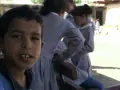 Un garçon souriant pose devant des filles en uniforme dans la même cour d'école.