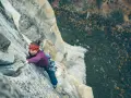 Babsi Zangerl klettert konzentriert eine steile Felswand empor, mit einem roten Stirnband und Kletterausrüstung.
