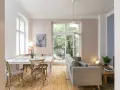Gemütliches 15 qm Wohnzimmer mit Essbereich einrichten: heller Esstisch, graue Stühle, Sofa, Holzboden, Fenster mit Blick ins Grüne.