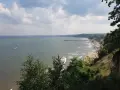 Widok z klifu orłowskiego na morze, plażę z ludźmi i molo. W oddali widać zarys wybrzeża.