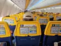 Widok wnętrza samolotu Ryanair z żółtymi oparciami siedzeń i instrukcjami bezpieczeństwa.