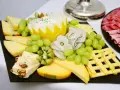 Plateau de fromage festif avec raisins verts, kiwi, noix et charcuterie. Une belle décoration plateau de fromage pour un événement.