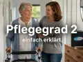Eine ältere Frau mit einem Gehwagen wird von einer jüngeren Frau gestützt. Der Text "Pflegegrad 2 einfach erklärt" ist prominent platziert.