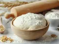 Ciasto na pyszną pizzę bezglutenową rośnie w drewnianej misce, obok wałka i mąki.