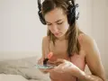 Dziewczyna w słuchawkach przegląda spotify lyrics na telefonie, zaznaczając fragmenty pomarańczowym pisakiem.