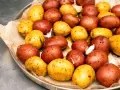 Ziemniaki z ogniska, czerwone i żółte, przyprawione czosnkiem i ziołami, gotowe do pieczenia.