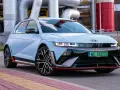 Jasnoniebieski Hyundai IONIQ 5 N z czarnymi akcentami i czerwonymi detalami, zaparkowany przed przemysłową instalacją.