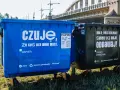 Niebieski kontener na makulaturę z napisem "czuję, że coś dla mnie masz. PAPIER" obok czarnego na odpady zmieszane.