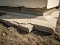 Popękane betonowe fundamenty domu, widoczne uszkodzenia i nierówności.