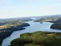 Rozległe jezioro raduńskie dolne otoczone lasami i polami. W oddali widać zabudowania.