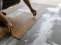 Hände legen Holzoptik-Vinylboden auf Kleber. Das Verlegen von Vinylboden erfordert Präzision.