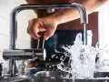 Mano girando la llave para cuidar el agua, que salpica al llenar un vaso.