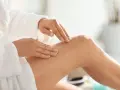 Kobieta w białym szlafroku wykonuje peeling nóg. To idealny peeling przed goleniem, by skóra była gładka.
