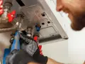 Tecnico con guanti lavora su una caldaia in blocco, avvitando un raccordo con un cacciavite.