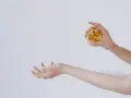 Dłoń trzymająca perfumy nad drugą dłonią.