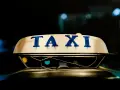 Tetto di un taxi con la scritta "TAXI" in blu. La luce soffusa e i riflessi suggeriscono la notte, un momento in cui ci si interroga quanto guadagnano i tassisti.