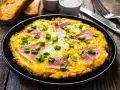 Pyszny omlet z szynką i serem, posypany szczypiorkiem, podany z grzankami. Idealny na śniadanie.