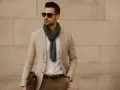 Uomo con blazer beige, sciarpa grigia e occhiali da sole. Un look elegante chic per un dress code uomo.