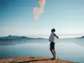 Mann mit ausgebreiteten Armen auf einem Felsvorsprung, der Rauch in den Himmel stößt. Ein Moment der Freiheit, wie Gottes Gunst.