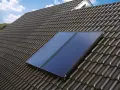 Deux panneaux de chauffage solaire thermique installés sur un toit en tuiles sombres, sous un ciel bleu.