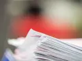 Stos dokumentów, potencjalne dowody rzeczowe w postępowaniu karnym, z czerwonym tłem.
