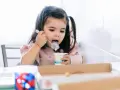 Mała dziewczynka z kitkami je jogurt z kubeczka. Od kiedy dziecko może jeść danonki? Odpowiedź jest prosta: gdy tylko zaczyna jeść pokarmy stałe.