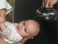 Chrzest dziecka. Woda spływa po głowie malucha w białej szatce. Niech to będzie początek mądrych życzeń na chrzest.