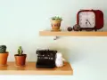 Ideas para decorar baldas salón: dos estantes de madera con cactus, una máquina de escribir antigua, un peluche blanco y un reloj rojo.