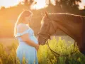 Une femme enceinte en robe bleue caresse un cheval brun au coucher du soleil. L'équitation enceinte est une belle façon de célébrer la maternité.