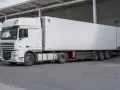 Biała naczepa chłodnicza z ciągnikiem DAF XF, gotowa do transportu.