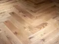 Tarima de madera en espiga, con nudos y vetas naturales, creando un patrón clásico y cálido.