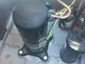 Close-up of an AC pump replacement in progress. A large black compressor sits on a gray base, connected to copper tubing and wires.