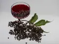Ein Glas tiefroter Holunderschnaps mit Rum, daneben frische Holunderbeeren und Blätter.