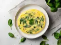 Delikatny omlet na parze ze szpinakiem, podany na talerzu, otoczony świeżymi liśćmi szpinaku i płatkami soli.
