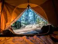 Vue de l'intérieur d'une tente orange, un feu crépite dehors. L'obligation sécurité camping est respectée avec ce campement bien installé.