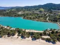 Turkusowa laguna na Kassandrze, otoczona zielonymi wzgórzami i lasem sosnowym. W oddali widać zabudowania i plażę z łodziami.