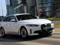 Białe BMW i4 w ruchu miejskim, z widocznymi światłami LED i grillem.