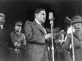 Un homme en costume parle à un microphone, entouré d'officiers en uniforme. Un moment clé de la dictature portugaise de Salazar.