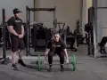 Kvinna förbereder sig för trap bar marklyft med en instruktör bredvid.