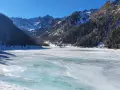 Il lago di Fontana Bianca, un'immensa distesa ghiacciata sotto un cielo azzurro, circondato da montagne innevate e boschi scuri.