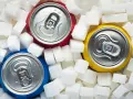 Trzy puszki napojów otoczone kostkami cukru. Obraz wizualizuje, ile cukru jest w coli, pokazując jego ogromną ilość.
