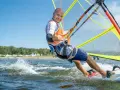 Mężczyzna na desce windsurfingowej, uśmiecha się i pokazuje kciuk w górę.