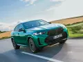 Zielony suv coupe pędzi po drodze, otoczony polami i błękitnym niebem.