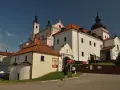 Białe budynki z czerwonymi dachami, wieże i kopuła tworzą malowniczy klasztor kamedułów.