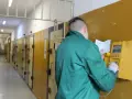 Więzień w zielonej kurtce korzysta z budki telefonicznej, sprawdzając książkę adresową. To dowód, że w więzieniu można mieć telefon, choć na określonych zasadach.