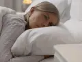 Kobieta w łóżku, zamyślona, zastanawia się co po menopauzie. Obok szklanka wody.