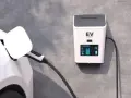 Biały samochód elektryczny podłączony do ładowarki EV na ścianie.