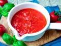 Frische Tomatensauce selber machen: Ein weißer Topf mit leuchtend roter Sauce, umgeben von reifen Tomaten und Basilikum auf einem Holzbrett.