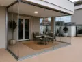 Terrazza moderna con vetrate Vepa scorrevoli, arredata con due poltrone, tavolino e tappeto. Piante in vaso e vista sui tetti.